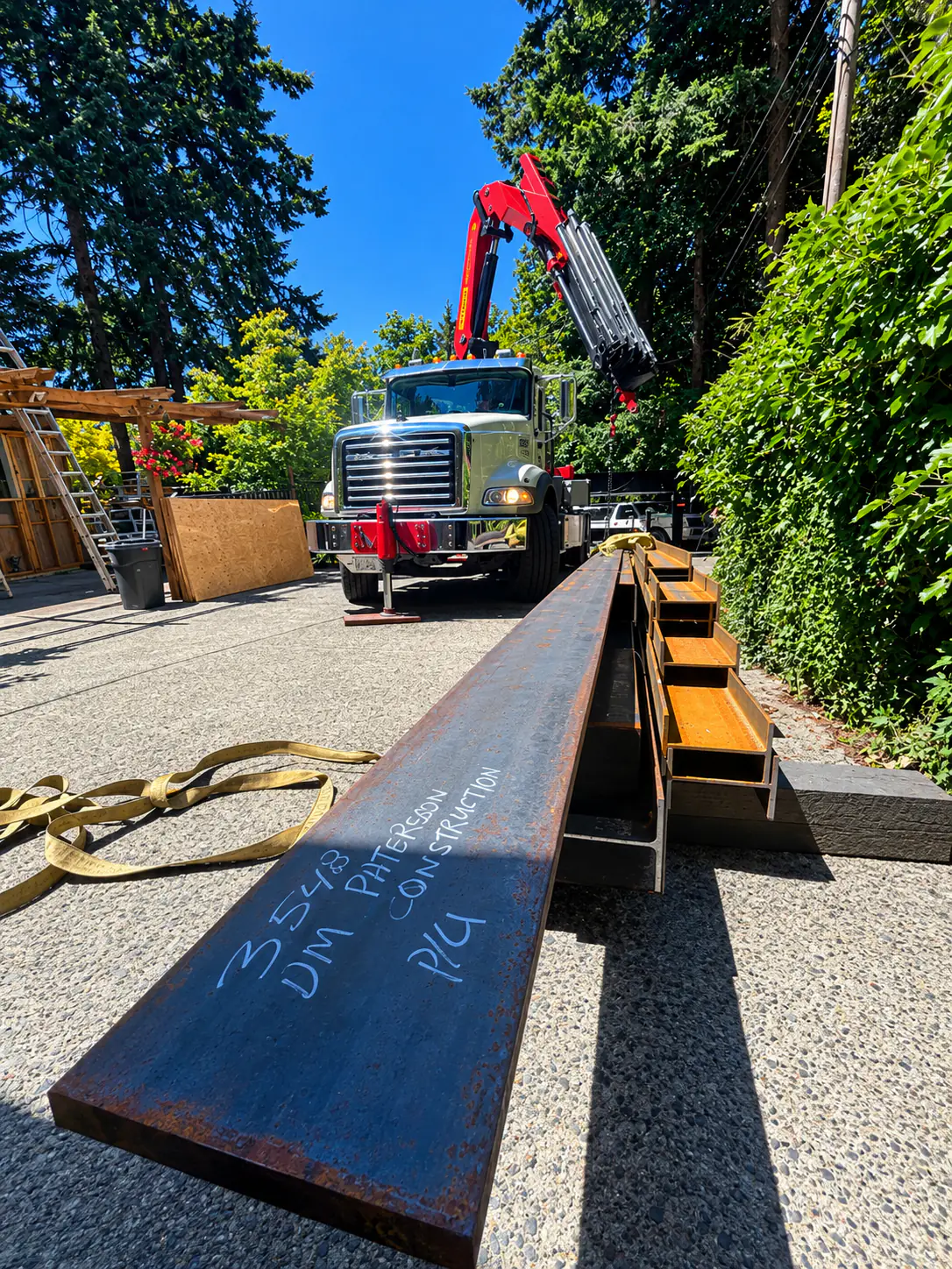 Steel beams stencilled DM Patterson Construction being offloaded by crane truck at a Vancouver Island job site