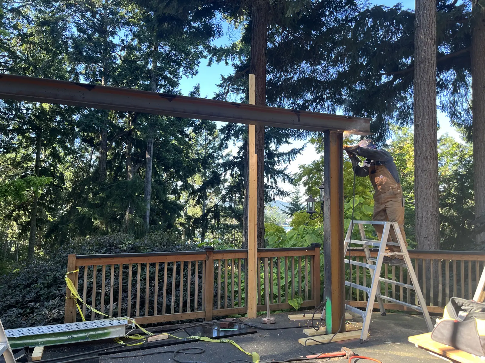 Worker installing a beam over a deck with a wooded outlook