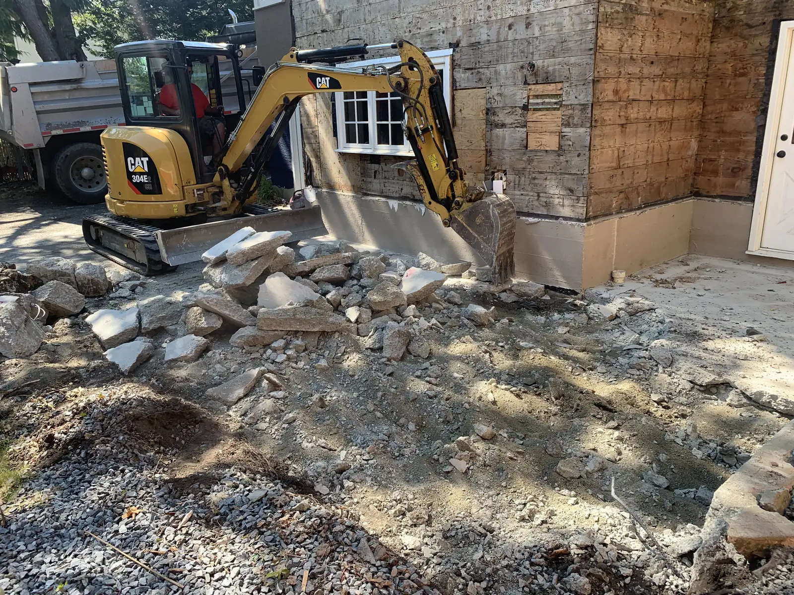 Excavator working on rock beside a house