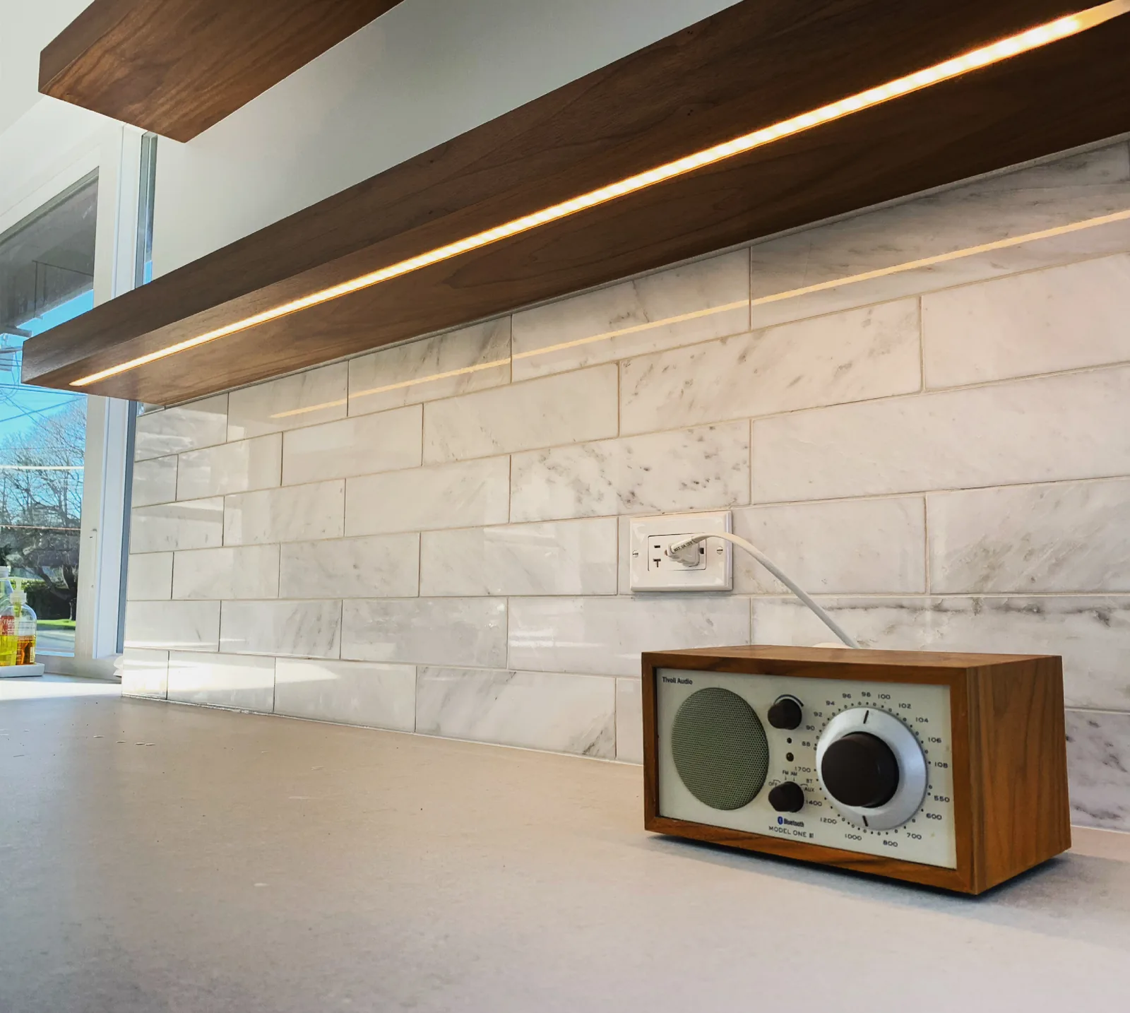 Marble tile backsplash with a wood floating shelf above a counter