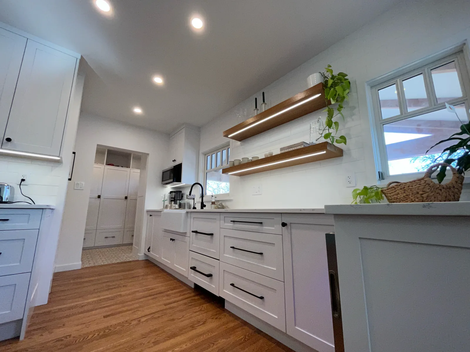 Kitchen with white cabinets, wood floating shelves and hardwood flooring