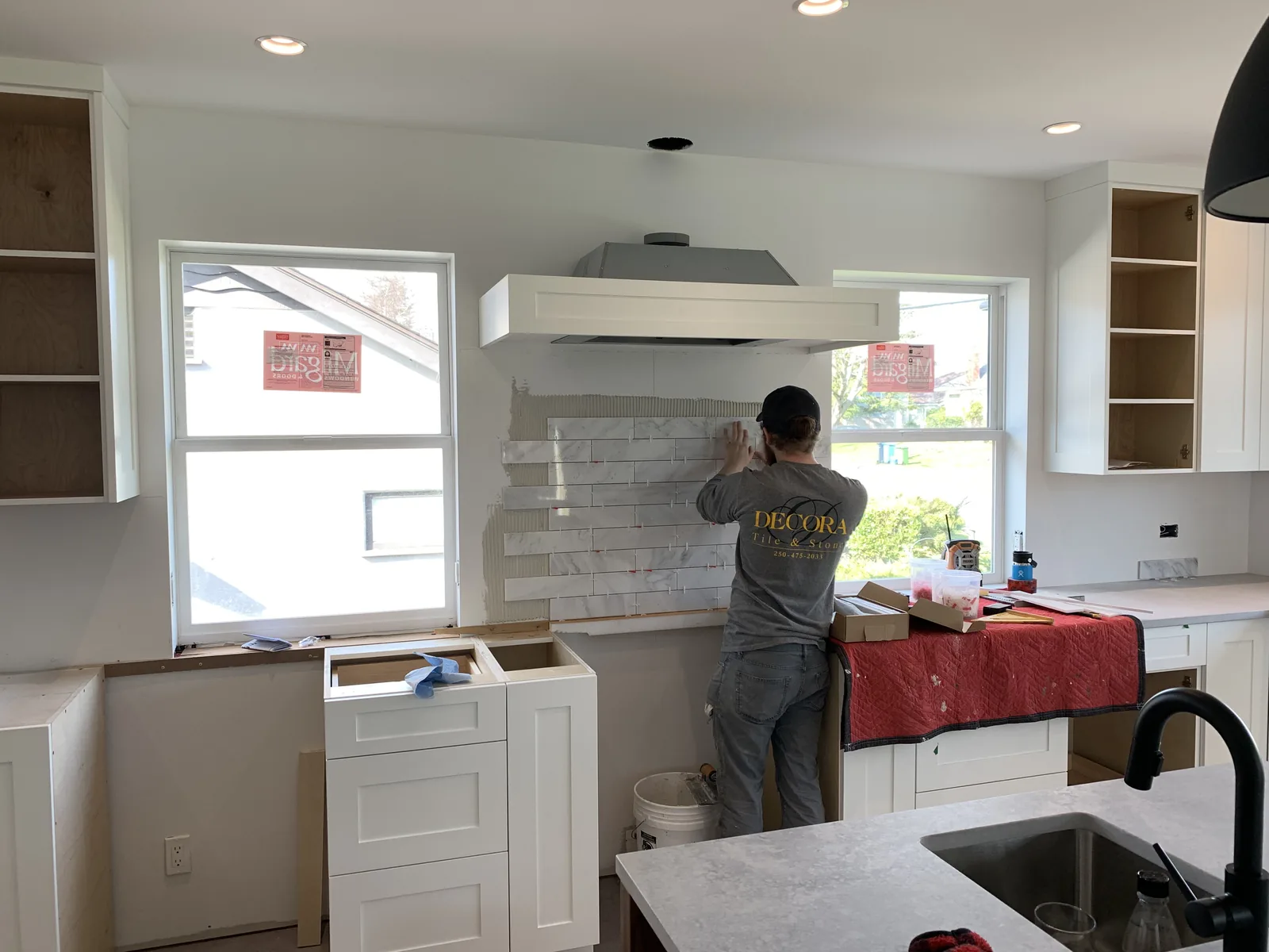 Tiler setting a marble backsplash above a range