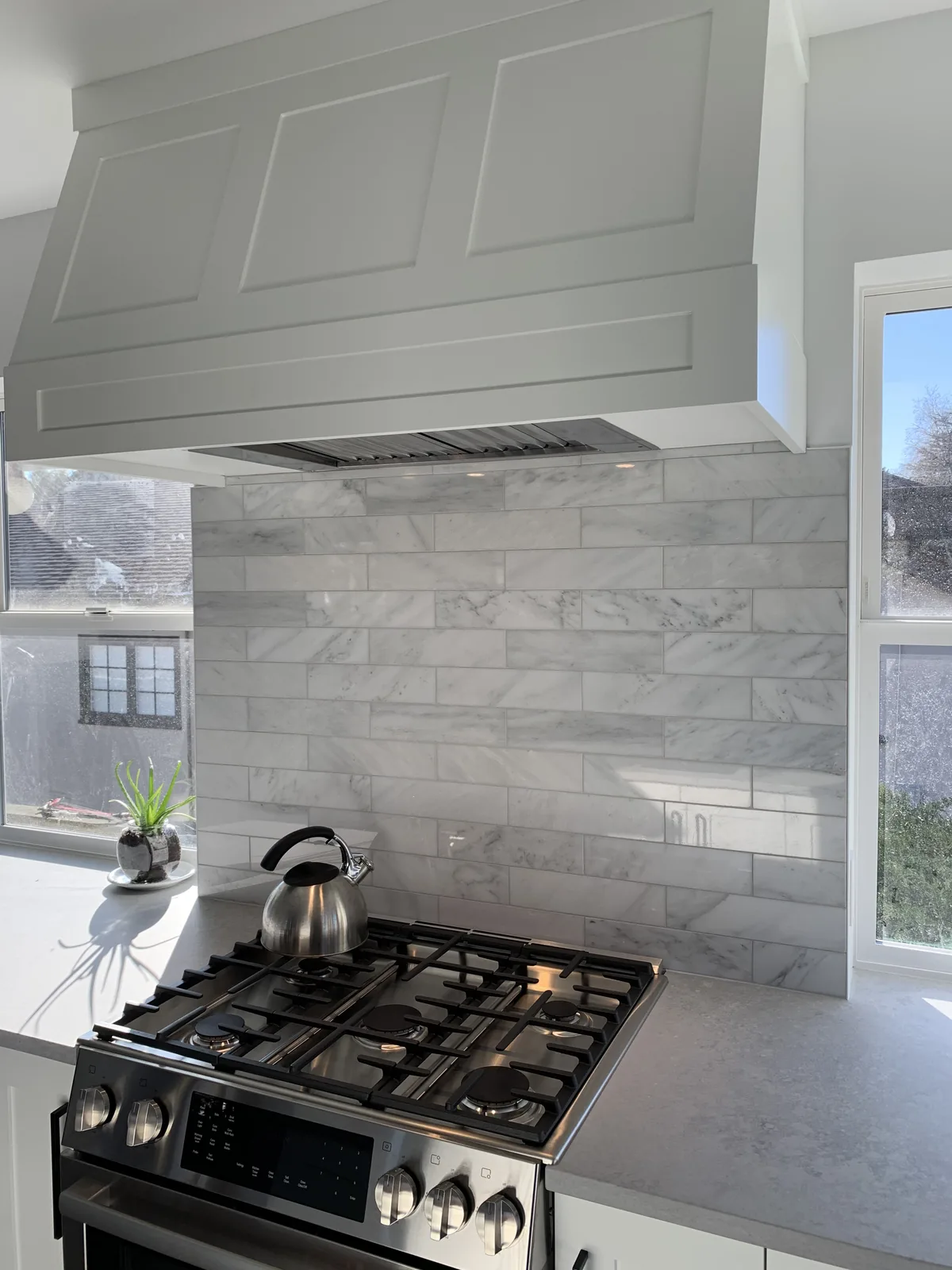 Range hood and marble backsplash above a gas range